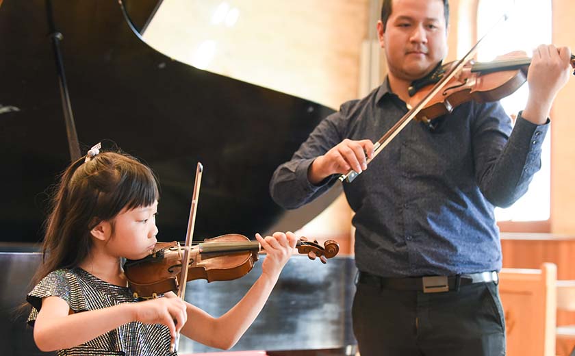 young girl and older male both playing violins in a concert performance